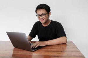 Young Asian man feeling happy and smile when work laptop on table. Indonesian man wearing blue shirt photo