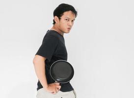 Young Asian man is angry and ready to strike with a frying pan. Indonesia Man wear black shirt Isolated grey background photo
