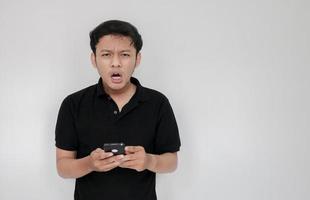 un joven asiático llora y se entristece cuando mira el teléfono inteligente. indonesia hombre usar camisa negra aislado fondo gris foto