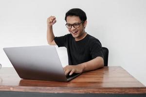 Happy excited Asian man with laptop and raising his arm up to celebrate success or achievement. photo