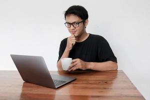 Young asian man is smile and enjoy when working at home with laptop and a cup of coffee. A man sitting on bed and working. Work from home concept photo