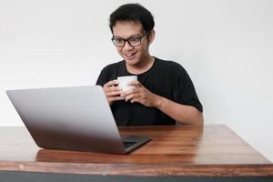 Young asian man is smile and enjoy when working at home with laptop and a cup of coffee. A man sitting on bed and working. Work from home concept photo