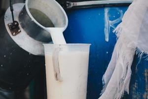 agricultor vertiendo leche cruda de la granja lechera en un recipiente para venderla a industrias o mercados foto