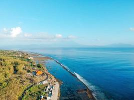 Photos are many people on the Sandy tropical beach with tree, umbrella, crystal clear sea, and white sand beach in Bali, Indonesia