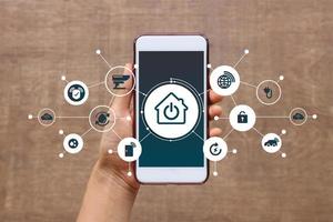 mano de mujer sosteniendo un teléfono inteligente en casa con íconos, estilo de vida de la persona en la vida moderna internet de las cosas, tecnología inteligente para el hogar. concepto de automatización. la nueva innovación del futuro foto