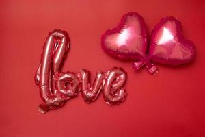 Festive background for Valentines Day from Foil balloons shape heart and love word on red background photo