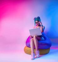 a woman in a bright bathing suit with blue hair is sitting on a chair bag with a laptop photo