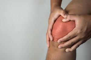 el hombre sostiene su punto de dolor en la articulación de la rodilla. el punto rojo muestra la posición de la lesión. primer plano de la vista frontal. foto