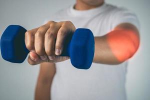 Tennis elbow concept. The man uses a blue dumbbell to physical therapy. Pain symptom area is shown with red color. Healthcare knowledge. Medium close up shot. photo