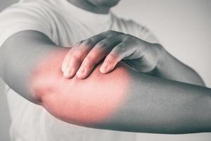 Lesión en el codo por tenis y golf. el hombre usa los dedos para masajear su brazo. el área de síntomas de dolor se muestra en color rojo. conocimiento sanitario. primer plano medio con espacio de copia. tono blanco y negro. foto