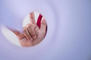 Hand sign of love looks through white paper sheet. This shot is focused on fingers. Valentine's concept with copy space. photo