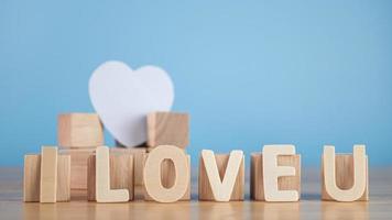 These words mean I LOVE U in wood plates. The square blocks support the white heart. Close up shot isolated on blue background. valentine's day concept. photo