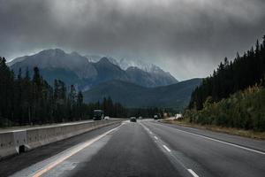 Car driving on highway with rocky mountains and moody sky in overcast day at Banff national park photo