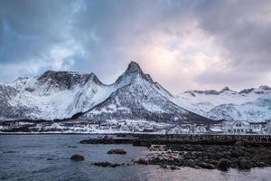 Scandinavian village on coastline with snowy mountain on background at Mefjord Brygge, Senja Island photo