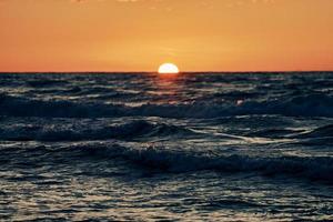 Half sun below horizon over blue sea waves, beautiful sunset over sea, breathtaking seascape photo