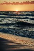 Beautiful sunset over sea waves, half sun below horizon, seacoast view, amazing seascape photo