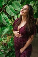 hermosa mujer embarazada sobre fondo de hojas verdes, hermosos ojos felices foto