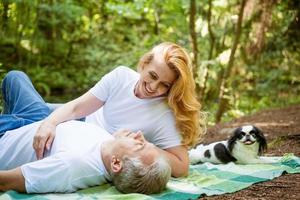 pareja madura en el bosque yacen sobre una manta con un perro foto