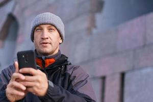 Portrait of happy smiling caucasian man with smartphone on city street against photo