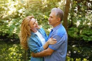 una pareja madura y feliz se para en el bosque en un día soleado y se abraza foto