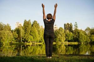 Adult woman doing exercises by the lake in the park during the day photo