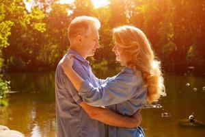 una pareja adulta se para en la orilla del lago en un abrazo en los rayos del sol poniente foto