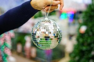 man's hand holds a Christmas tree toy disco ball, a holiday decoration photo