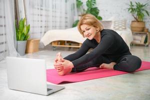 Fitness training online, senior woman at home with laptop photo
