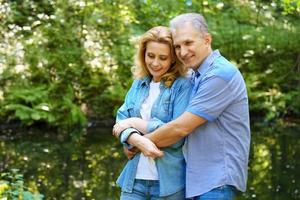 una pareja madura y feliz se para en el bosque en un día soleado y se abraza foto