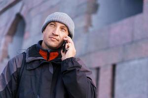 Portrait of happy smiling caucasian man with smartphone on city street against photo