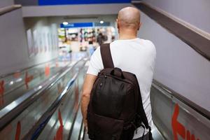 Bald man walking down the escalator with a backpack photo
