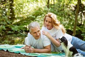 pareja madura en el bosque yacen sobre una manta con un perro foto