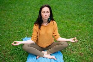 A lovely woman meditates sitting on the green grass in the Park photo