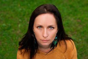 Close-up portrait of a woman with dark hair and blue eyes against a background of green grass photo