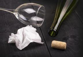 The used white crumpled paper napkin and an empty wine bottle with cork on old wooden table photo