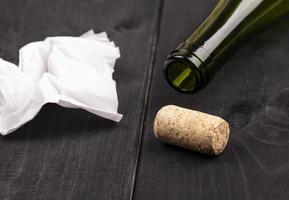 The used white crumpled paper napkin and an empty wine bottle with cork on old wooden table photo