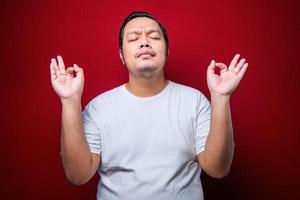 Young asian man wearing white t-shirt relax and smiling with eyes closed doing meditation gesture with fingers. Yoga concept. photo