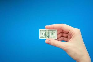 mano de mujer sosteniendo un billete pequeño de 100 dólares estadounidenses, fondo azul foto