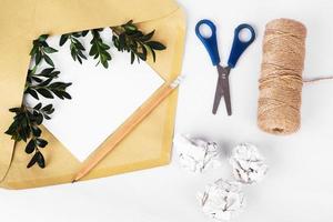 Craft paper envelope with empty paper and green twigs among crumpled paper and bundle winding on white background photo