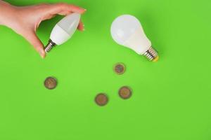 energy-saving lamps in the hand and euro coins on a green background. top view. Energy savings concept. Place for text photo