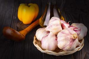 The garlic in a basket with yellow pepper and a wooden spoon on an old wooden table photo