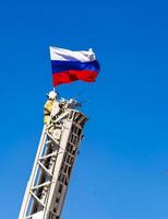 el bombero asegura una bandera rusa en la escalera de incendios en el fondo del cielo azul foto