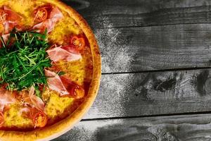 pizza italiana con jamón, tomates y hierbas sobre una mesa de madera foto