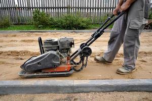 worker rams the ground with a vibrating machine.Side view. photo