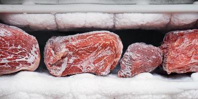 Large pieces of red meat in a freezer with a big quantity of frozen ice and snow photo