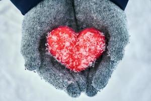 manos femeninas en guantes de lana con corazón de lana roja con copos de nieve al aire libre foto