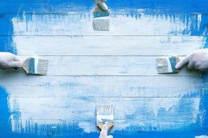Creative background with four hands painting blue wooden boards with white paint photo