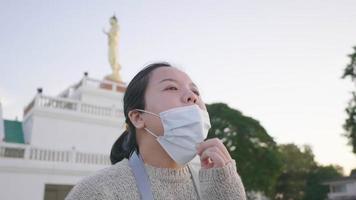 gros plan sur une femme asiatique debout et respirant profondément au parc, en sortant un masque et en prenant de l'air frais. fond de rivière et d'arbres, à la recherche d'une belle vue video