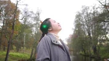 femme asiatique debout, regardant autour et prenant une profonde respiration dans la forêt, saison d'automne, feuilles tombant des arbres, belle nature, prendre de l'air frais au parc, suède video