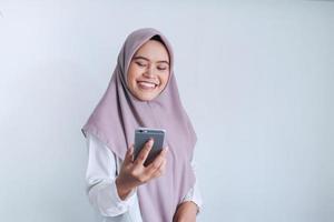 Young Asian Islam woman wearing headscarf is smile and happy in what she see on the smartphone. Indonesian woman on gray background photo